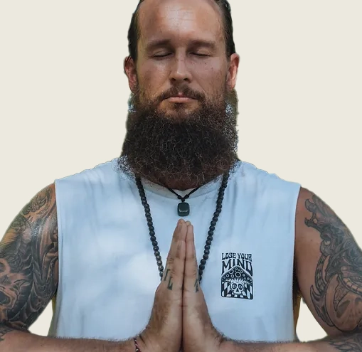Bearded man meditating, tattooed arms, white vest.